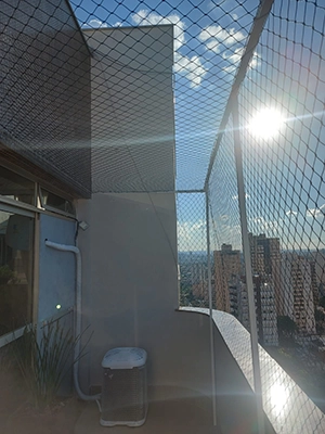 imagem de uma sacada, protegida com rede e estrutura, com o sol brilhando ao fundo